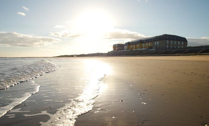 Looking up at The Beaches Hotel from Barkby Beach. Image shows the sand and the waves on the shore, and the hotel in the background.